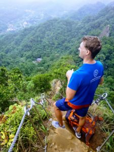 Guy on top of a rock observing the green nature in front